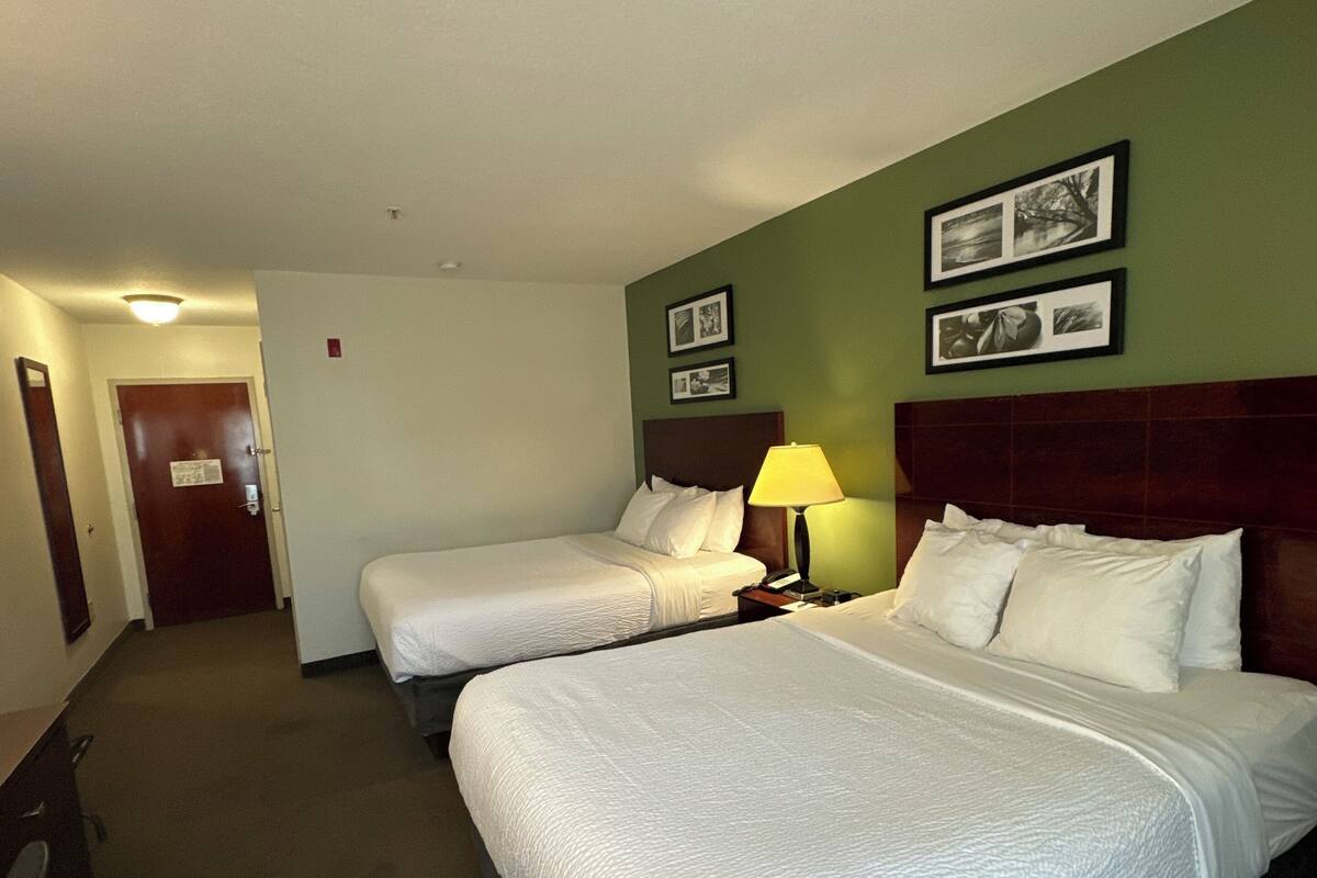 A hotel room with two beds, a nightstand with a lamp, and a door leading to another room.