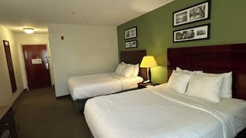 Una habitación de hotel con dos camas, una mesita de noche con lámpara y una puerta que da a otra estancia.