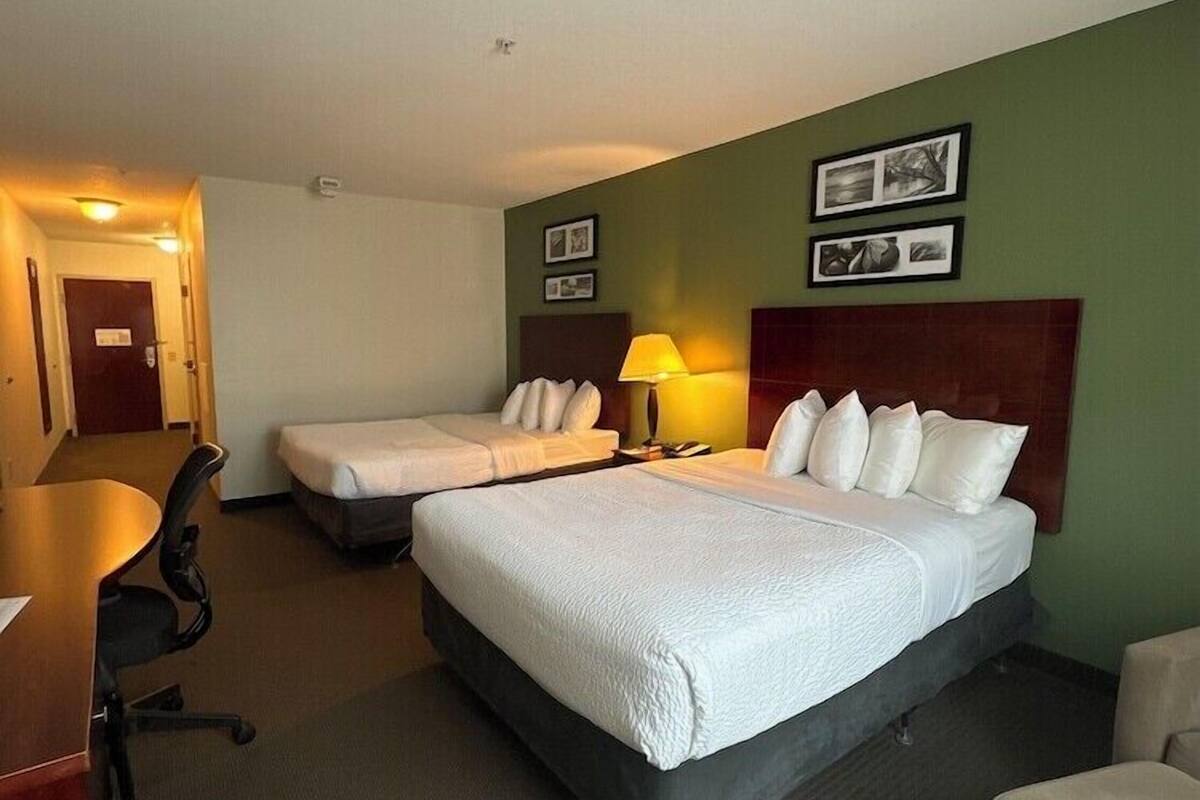 A hotel room with two beds, a desk, a chair, and a lamp.