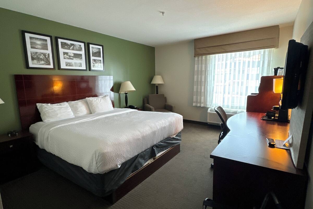 A hotel room with a bed, desk, chair, lamp, and framed pictures on the wall.