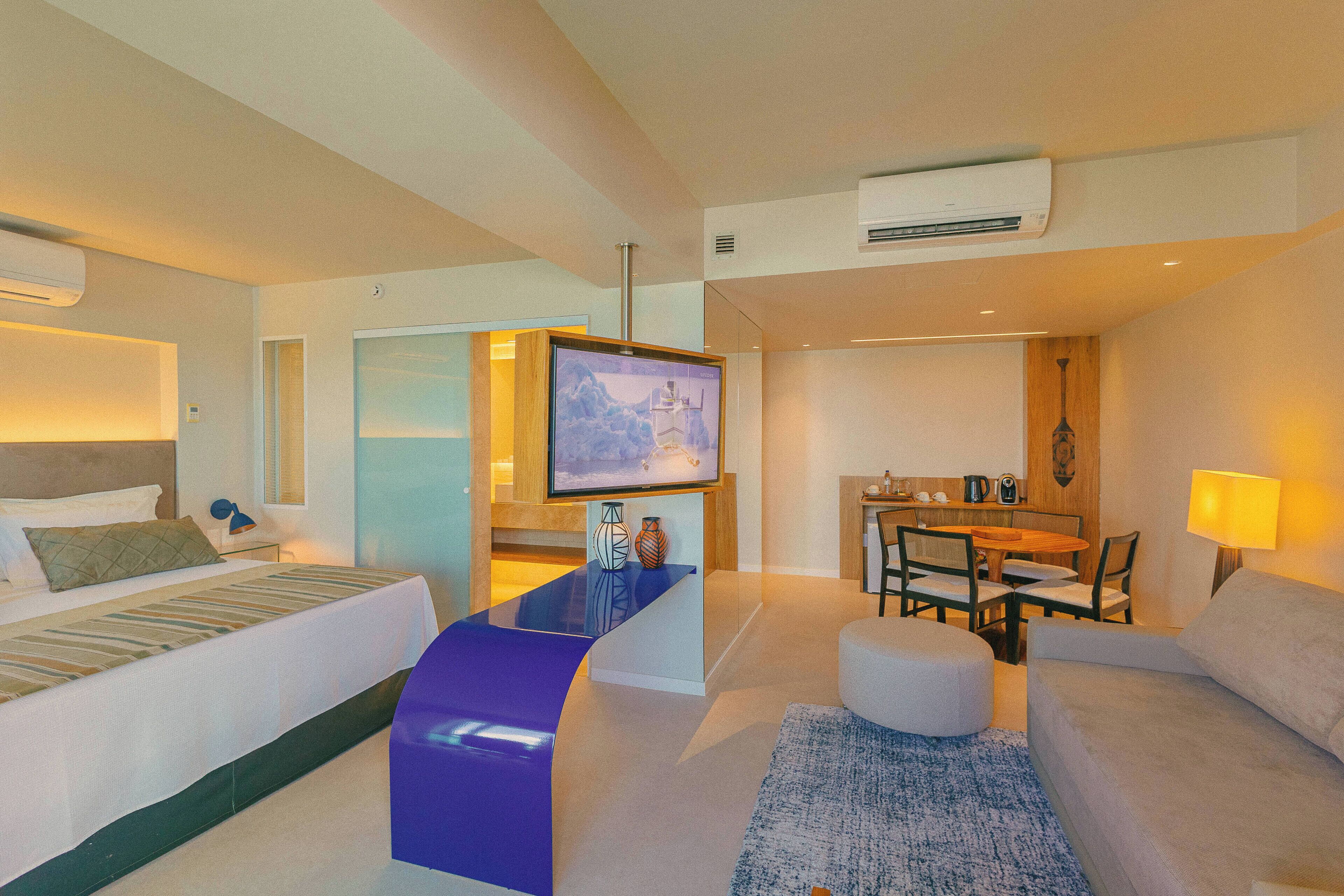 Una habitación de hotel moderna con cama, sofá, zona de comedor y televisor.
