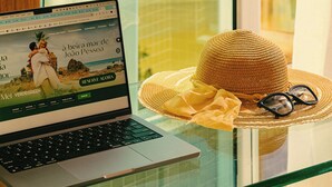 Una computadora portátil sobre una mesa de vidrio, con un sombrero de paja y unas gafas de sol a su lado.