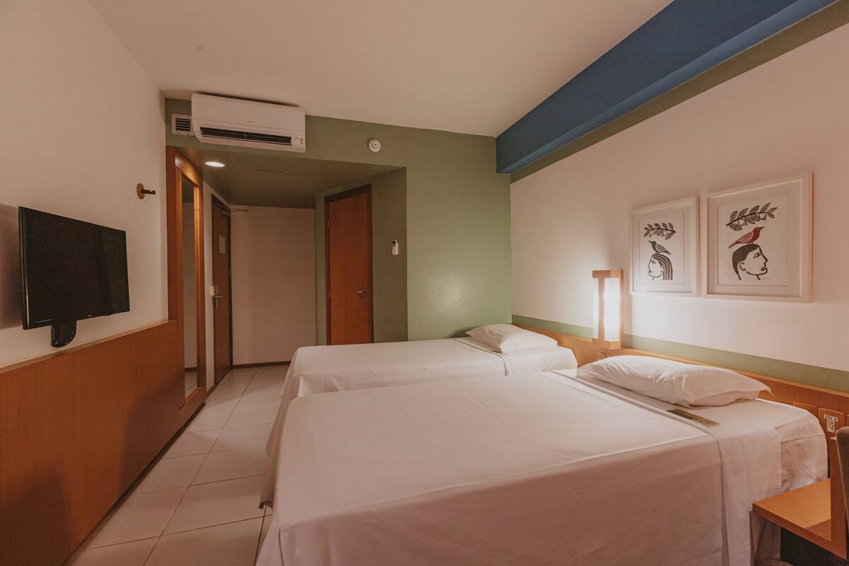 Habitación de hotel con dos camas, televisión y obras de arte en la pared.