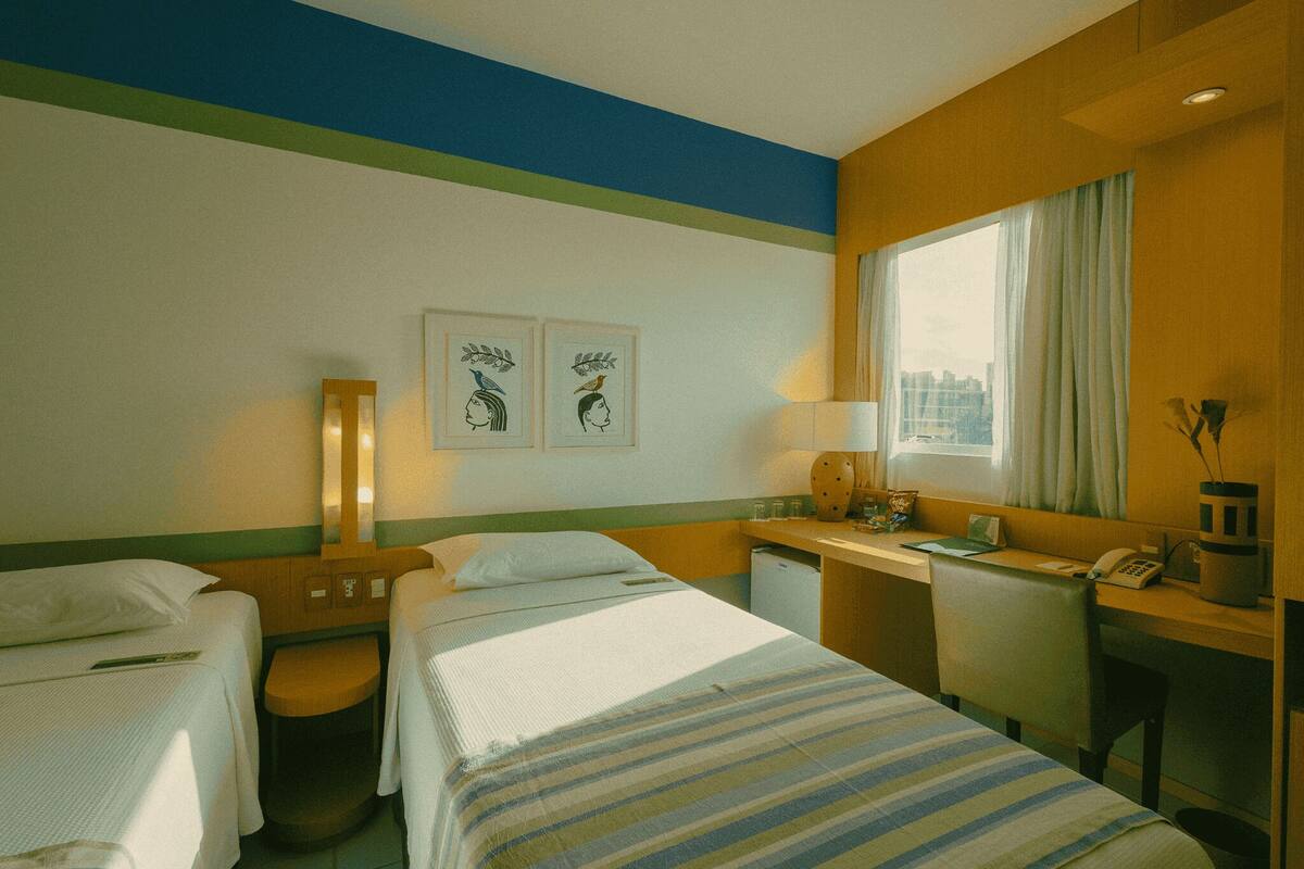 Habitación de hotel con dos camas, un escritorio, una silla, una lámpara y dos cuadros en la pared.