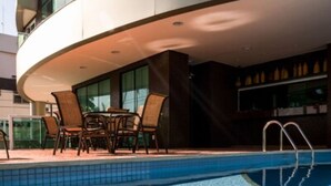 Una piscina con borde de baldosas, rodeada por un edificio moderno con amplias ventanas y un balcón curvo.