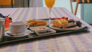 Bandeja de desayuno con tostadas, fruta y jugo sobre una mesa con vista al mar.