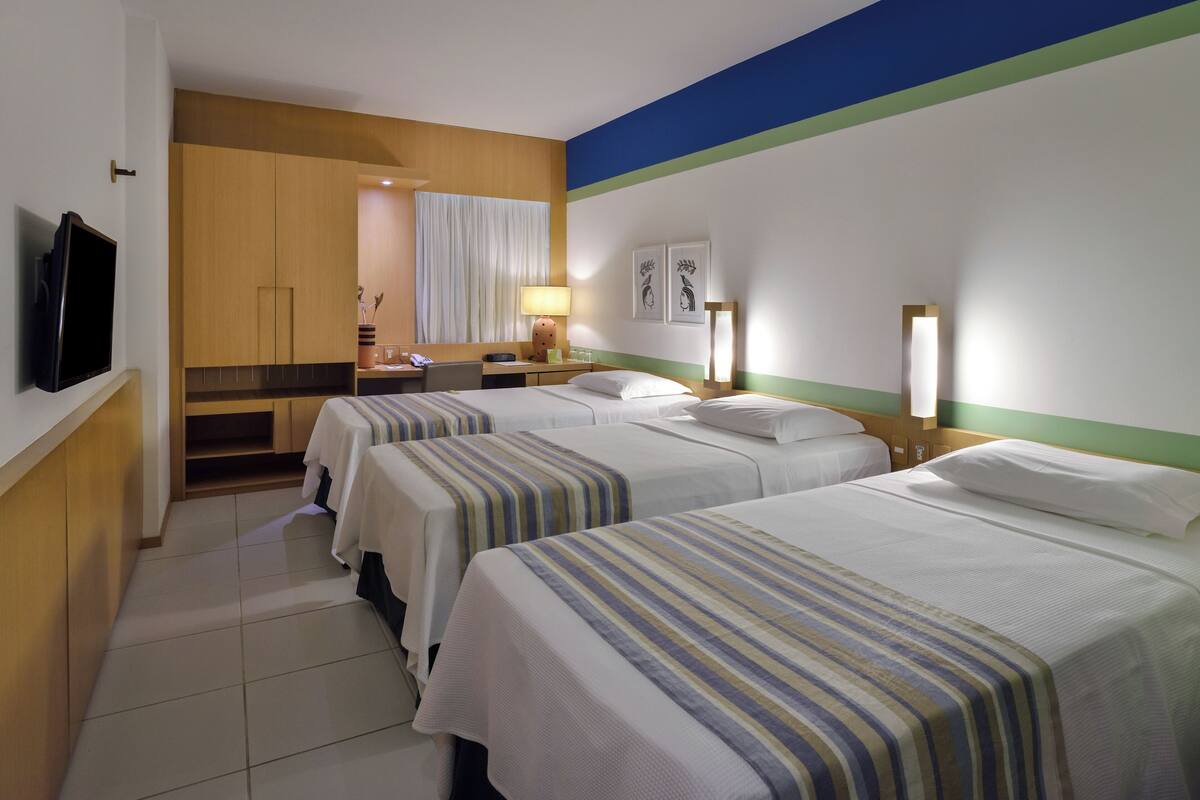 Una habitación de hotel con tres camas, televisión, escritorio y baño con ducha.