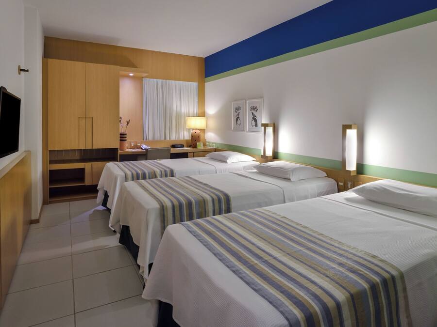 Een hotelkamer met drie bedden, een televisie, een bureau en een badkamer met douche.