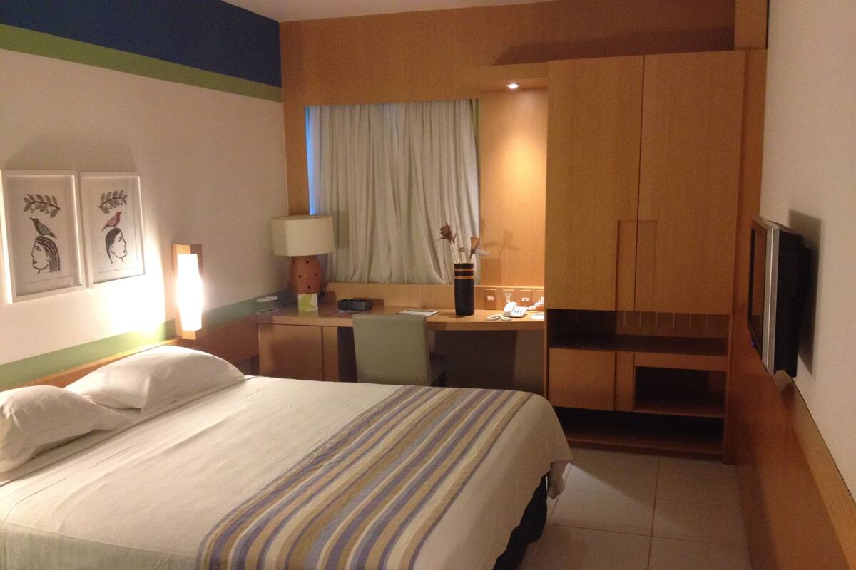 Habitación de hotel con cama, escritorio, silla y televisión.