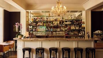 A bar area with a chandelier, multiple shelves of liquor bottles, and bar stools.
