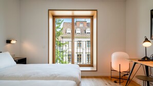 A bedroom with a large window, a bed, a desk, and a chair. - Der Teufelhof Basel (Basel)
