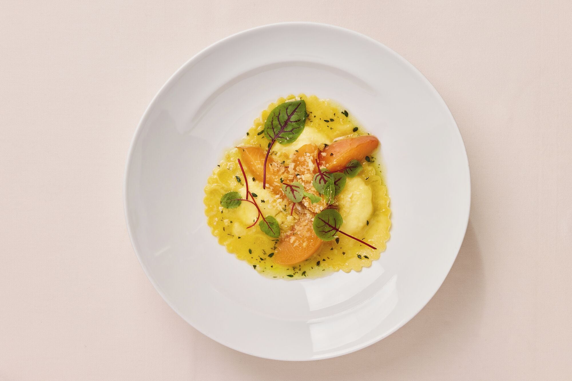 A white plate with a dish of yellow food, garnished with green leaves and red stems.