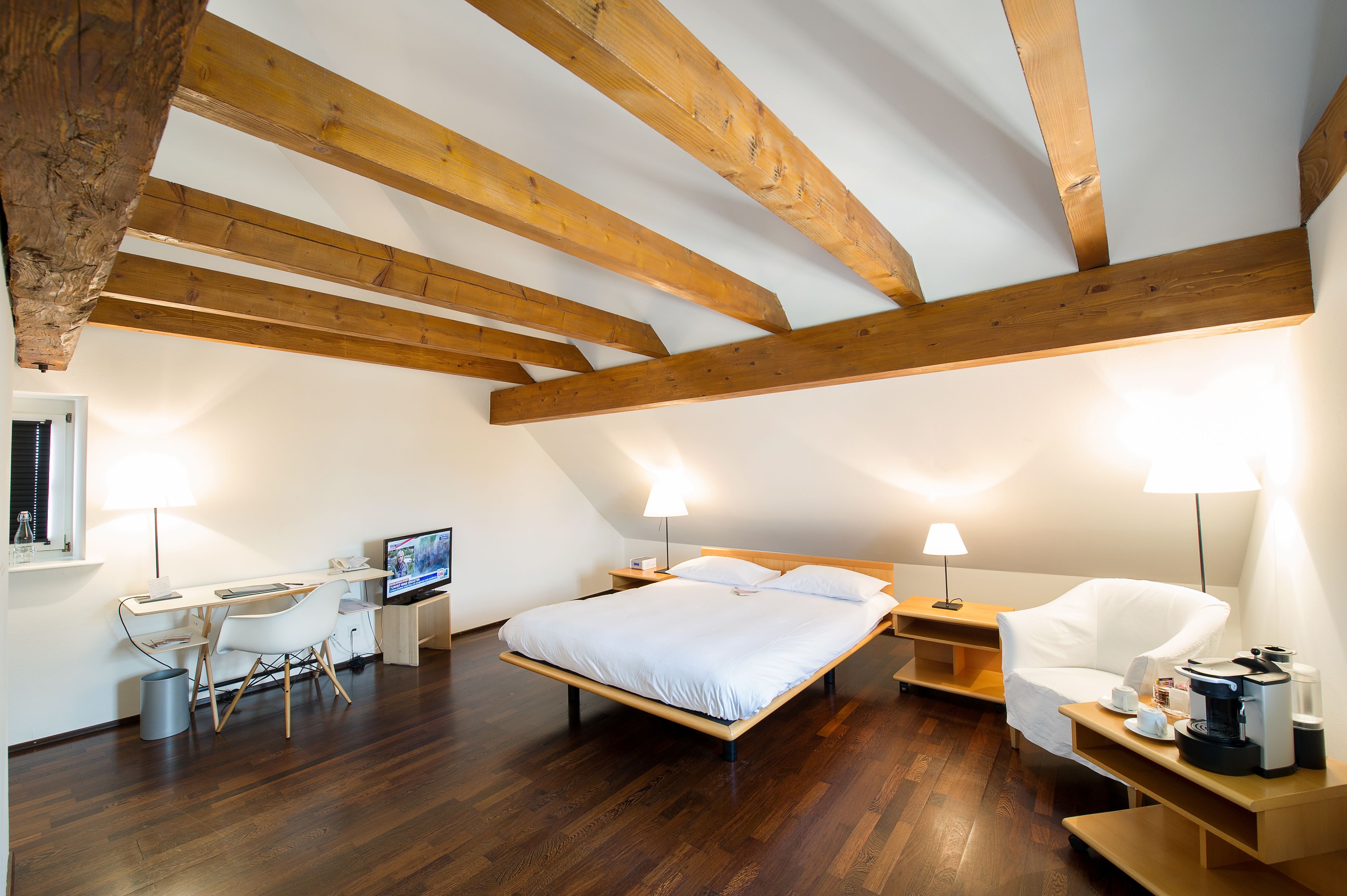 Ein Schlafzimmer mit Holzbalkendecke, einem Bett, einem Schreibtisch mit Computer und einem Stuhl.