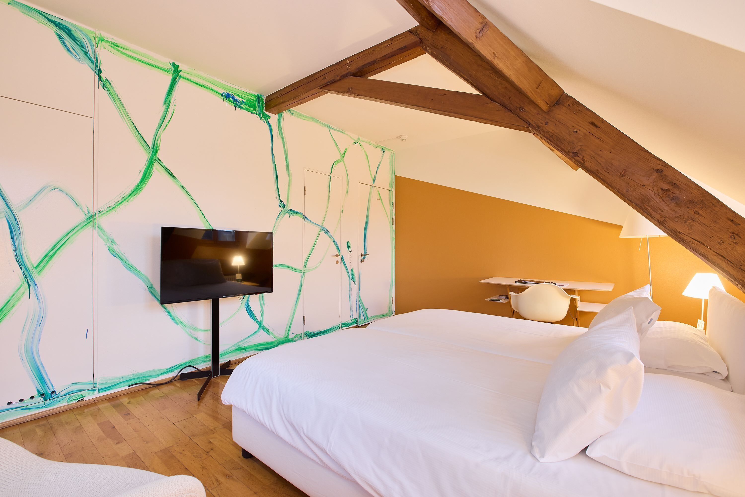 Un dormitorio con cama, televisor de pantalla plana y pared con pintura verde abstracta.