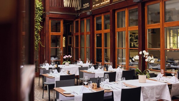 An outdoor dining area with tables set for two, large windows, and a wooden facade. - Der Teufelhof Basel (Basel)