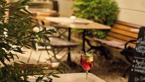 A patio area with tables and benches, a glass of red drink, and greenery. - Der Teufelhof Basel (Basel)