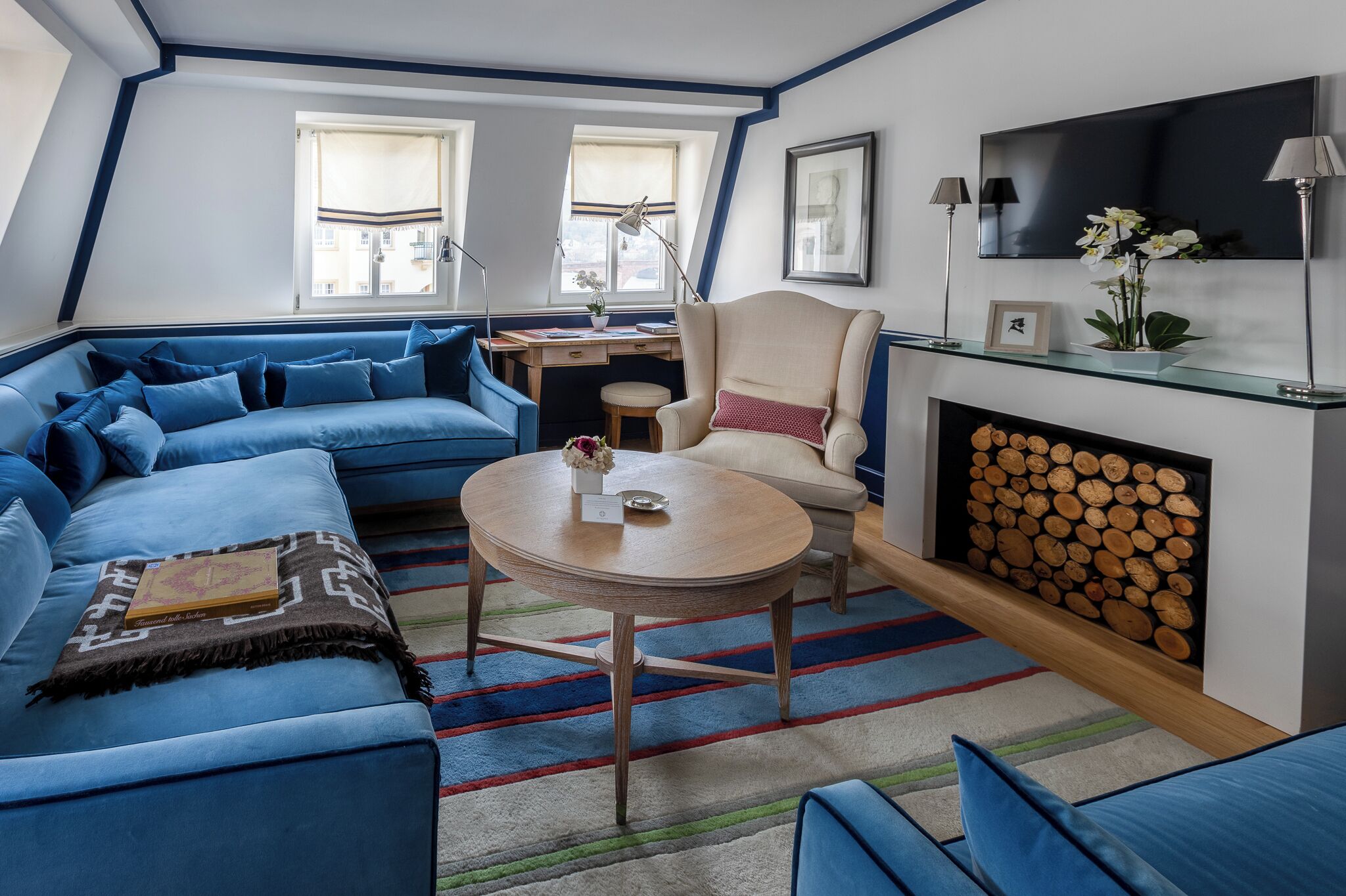 Ein modernes Wohnzimmer mit einem blauen Sofa, einem runden Couchtisch, einem Kamin und einem an der Wand befestigten Fernseher.