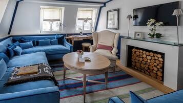 Ein modernes Wohnzimmer mit einem blauen Sofa, einem runden Couchtisch, einem Kamin und einem an der Wand befestigten Fernseher.