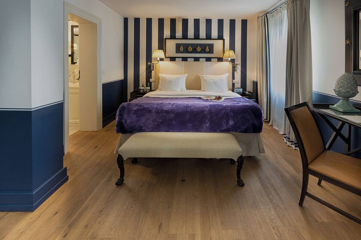 A bedroom with a bed, bedside tables, a bench, a chair, and a desk with a lamp.