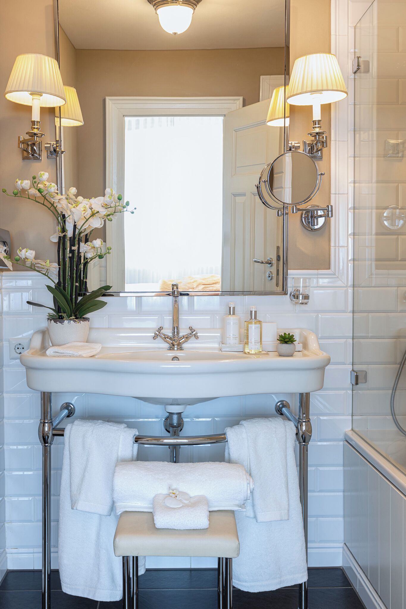 A bathroom with a white sink, two mirrors, a towel rack, and a potted plant.