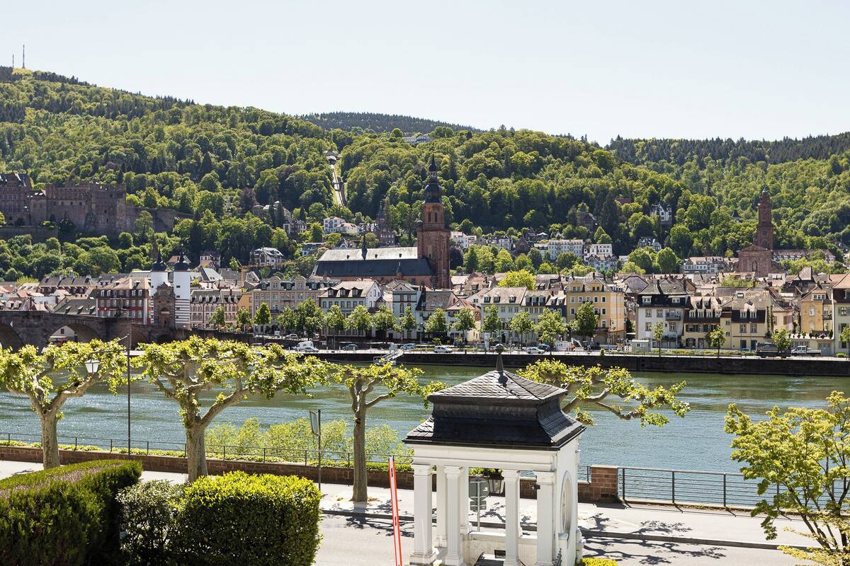 A riverside view of a town with historic buildings, a prominent church, and a small pavilion.