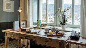 Een netjes opgeruimd bureau met een boek, een theepot, een schaal fruit, een vaas met bloemen en een telefoon.
