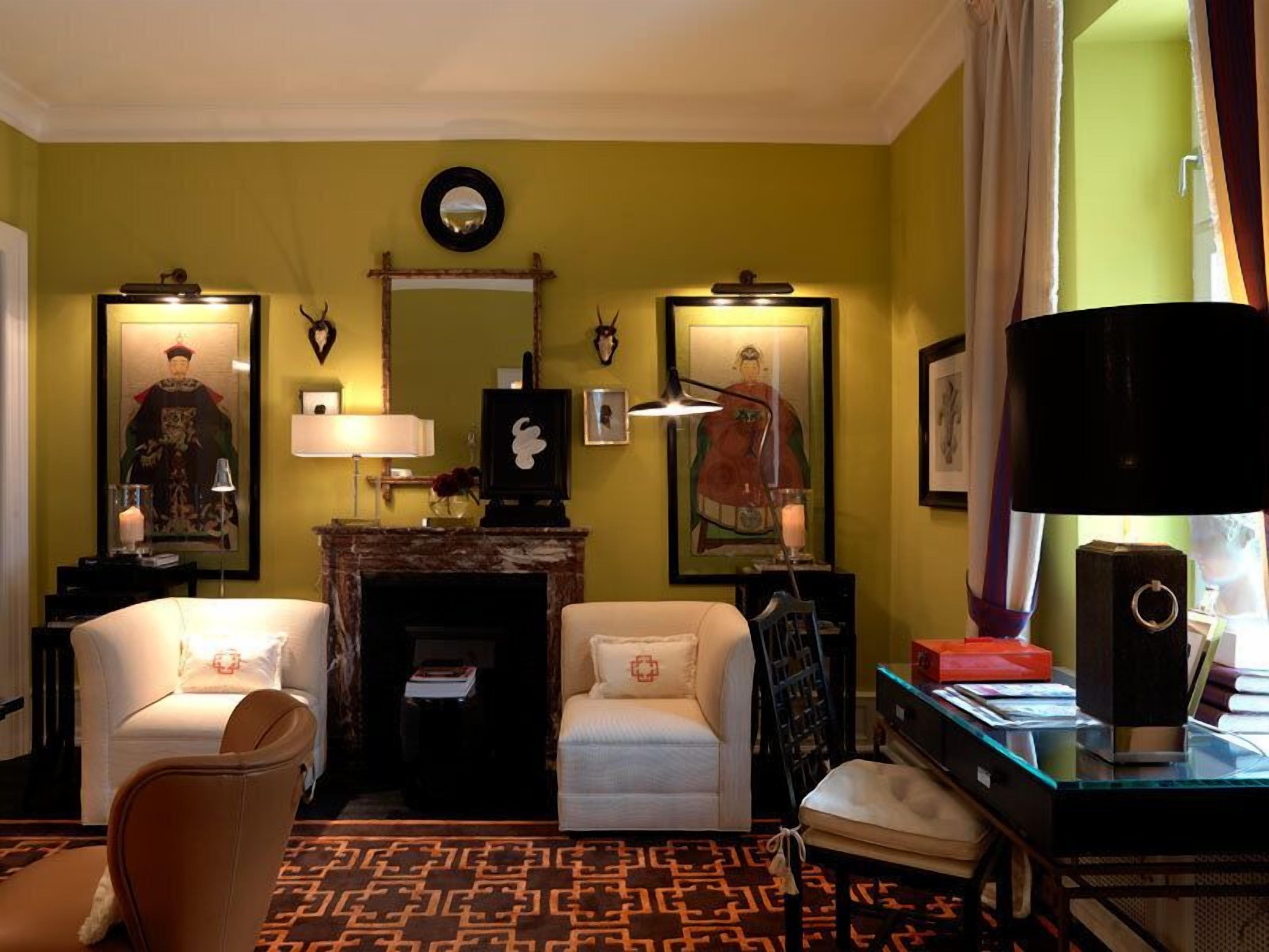 A room with two white sofas, a fireplace, framed artwork on the walls, and a desk with a computer and books.