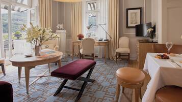 Une chambre d’hôtel dotée d’une grande fenêtre, d’un bureau, d’une chaise, d’une table à manger recouverte d’une nappe blanche et d’un banc rouge avec un coussin.