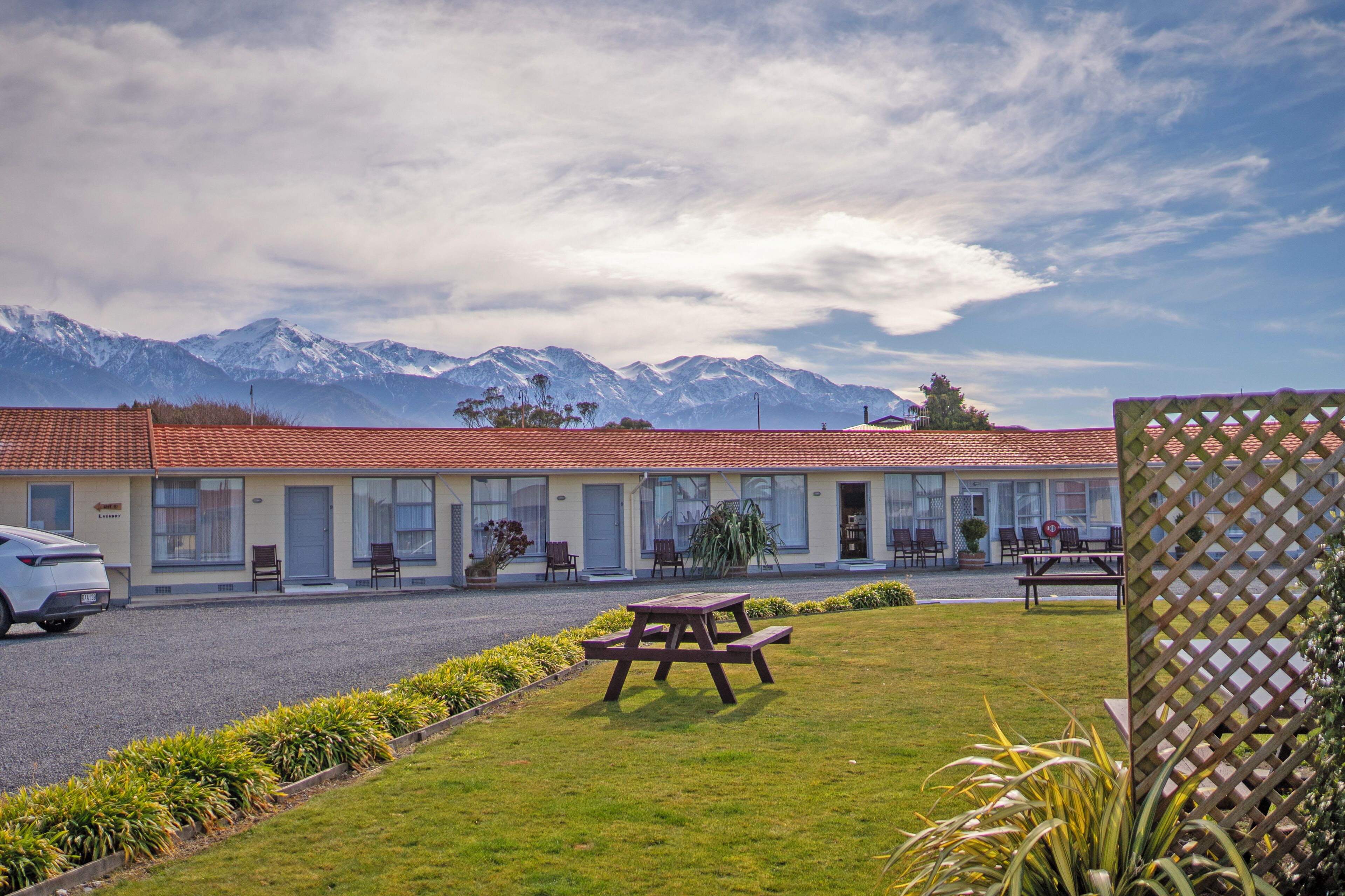 A motel with a red-tiled roof, a picnic table, and a view of snow-capped mountains.