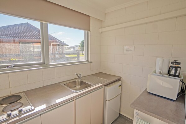 Cocina compacta con lavamanos, estufa, refrigerador y ventana con vista a una zona residencial.