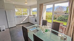 A modern kitchen with a glass dining table, white cabinets, and a view of mountains and greenery.