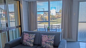 A modern living room with a grey sofa, floral cushions, and a view of a dining area through large windows.
