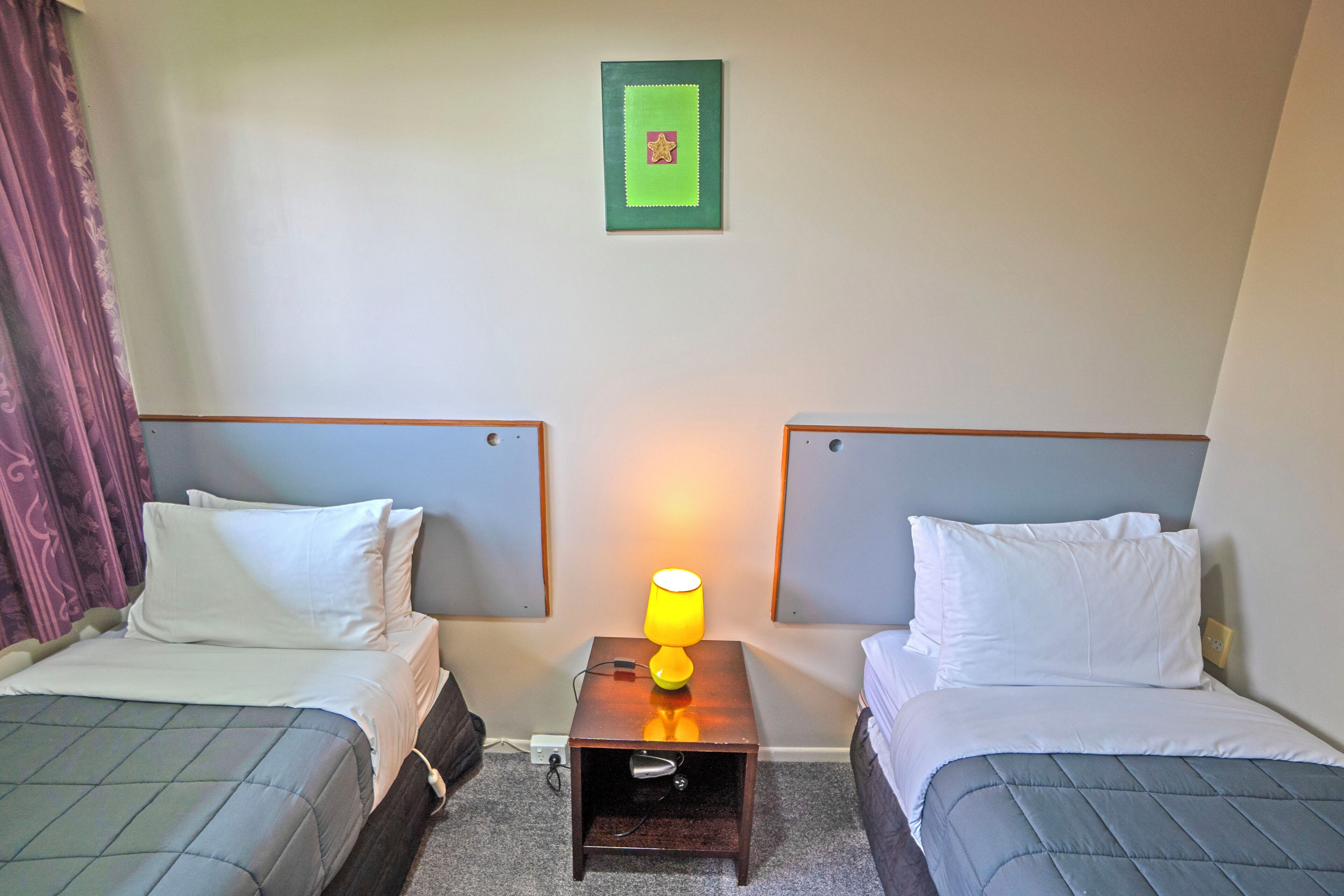 Habitación de hotel con dos camas, una mesita de noche con lámpara y una pequeña mesa.