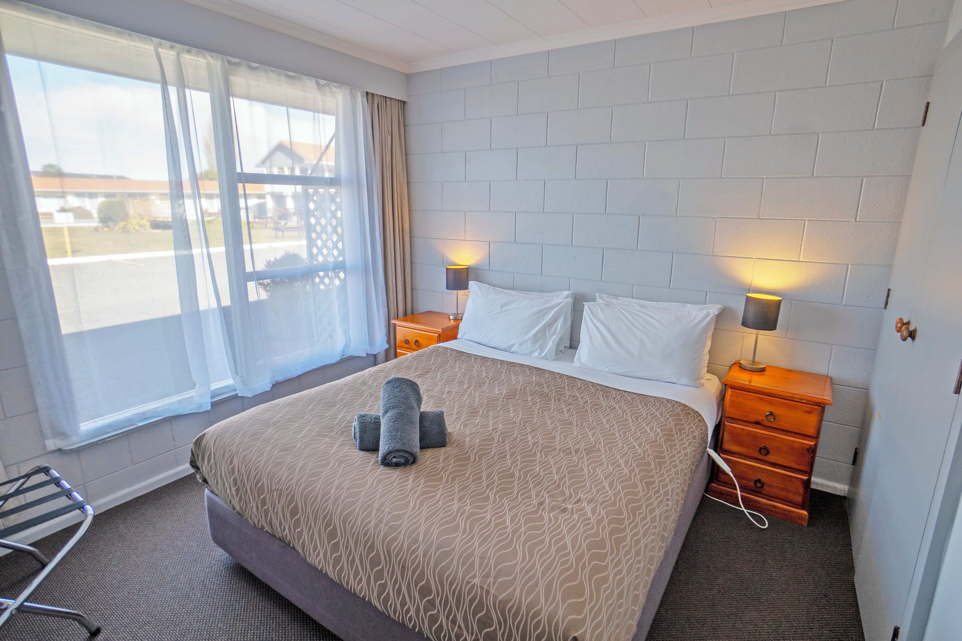 A hotel room with a large bed, two bedside tables with lamps, a window with curtains, and a view of the outside.