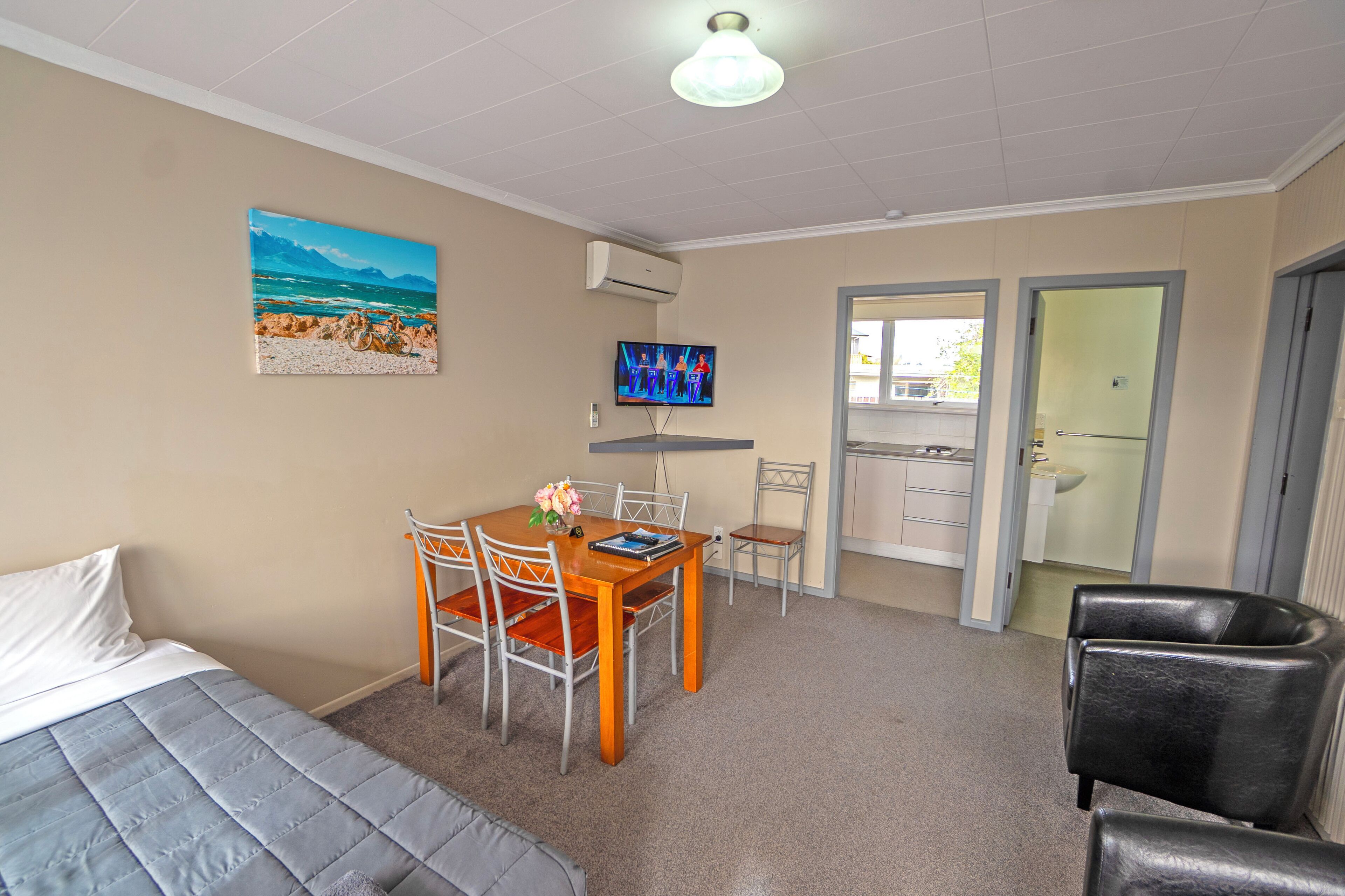 A room with a bed, a dining table with chairs, a TV, and a bathroom door.
