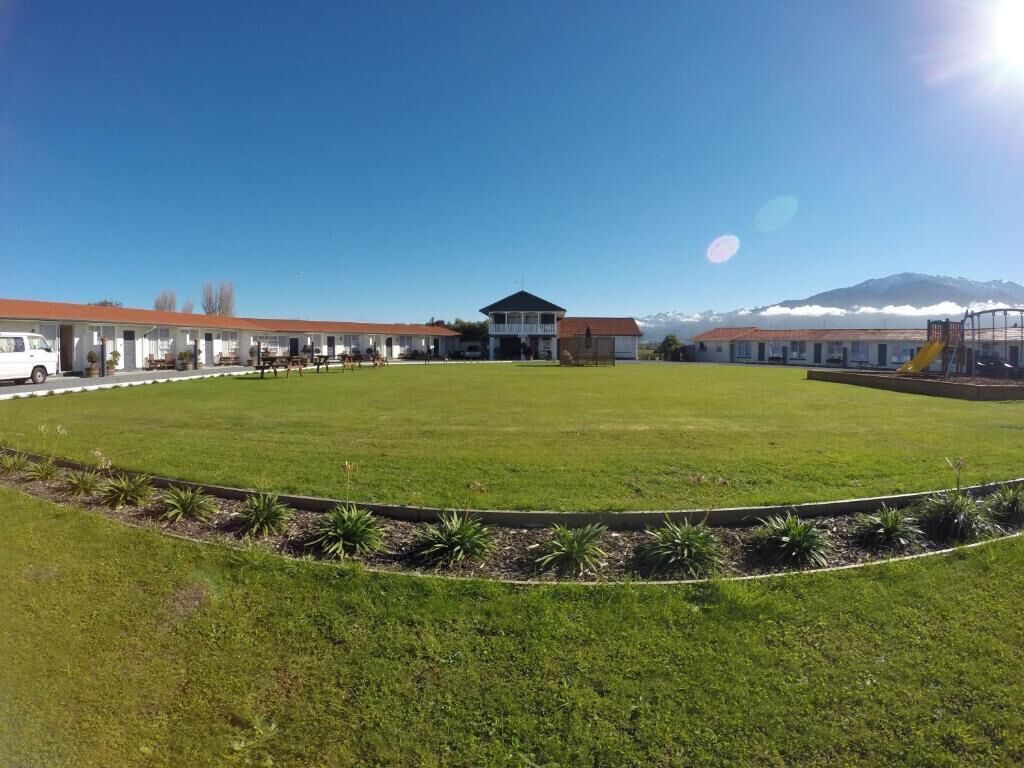 Un motel con un edificio central, un amplio césped y una montaña al fondo.