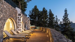 Una terraza de madera con sillones de descanso, paredes de piedra y vistas a pinos.