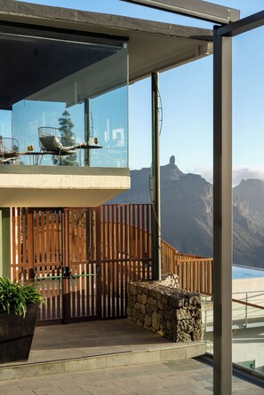 A modern balcony with a glass railing, a stone wall, and a wooden fence. - Parador de Cruz de Tejeda (Vega de San Mateo)
