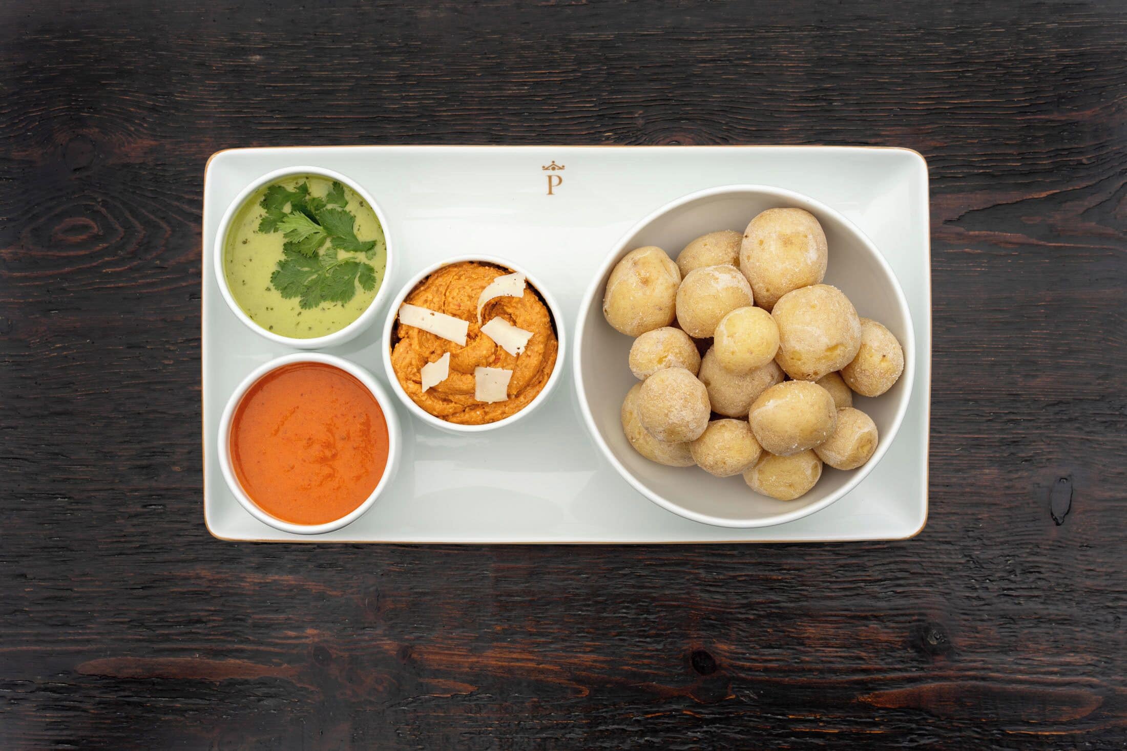 A white rectangular tray with three bowls of food on a dark wooden table.