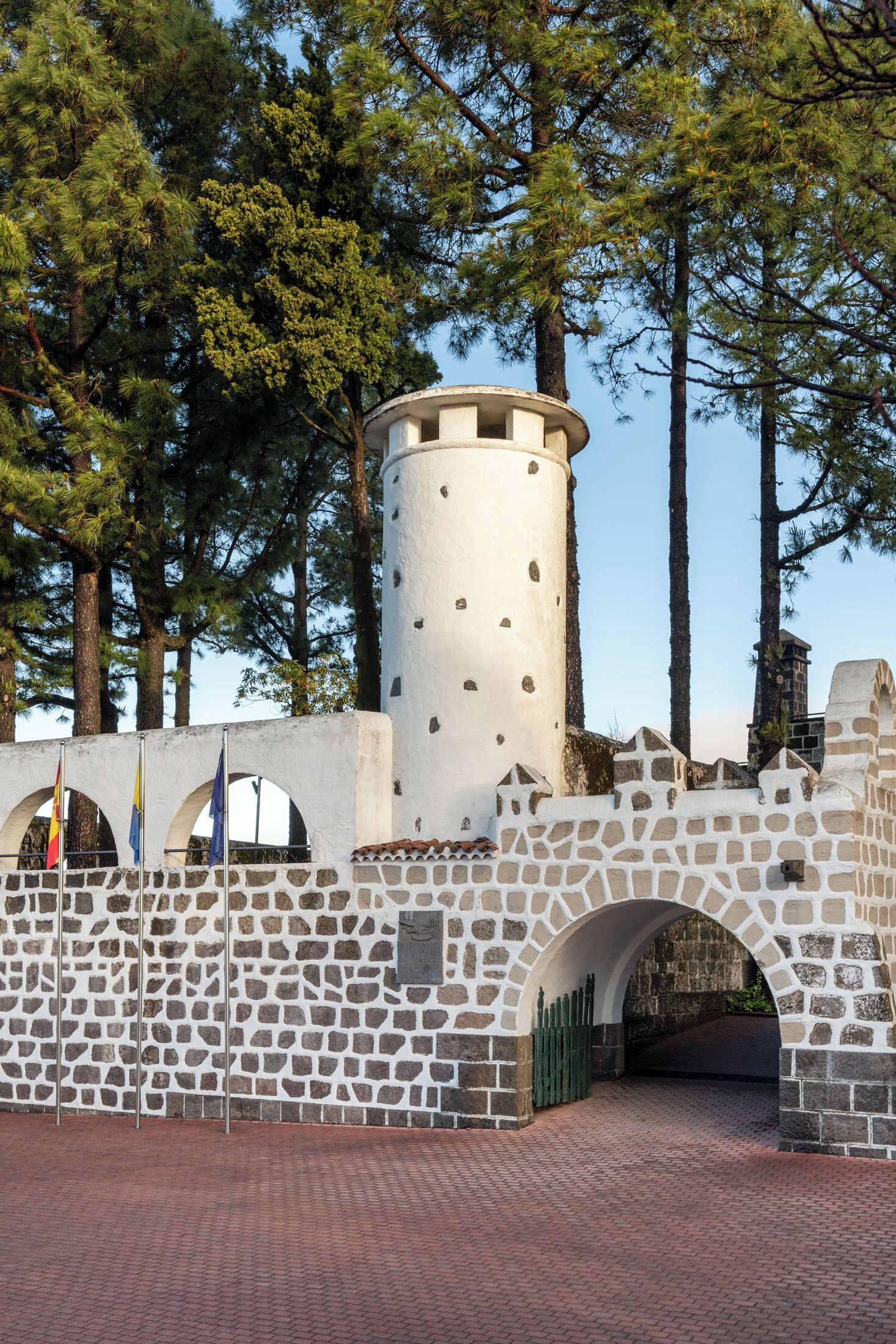 Een stenen toren met een cilindrische top, omgeven door een stenen muur met boogvormige openingen en een pad van baksteen.