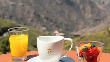 Une table avec un verre de jus d’orange, une tasse blanche, un verre de fruits, un biscuit et un beignet.