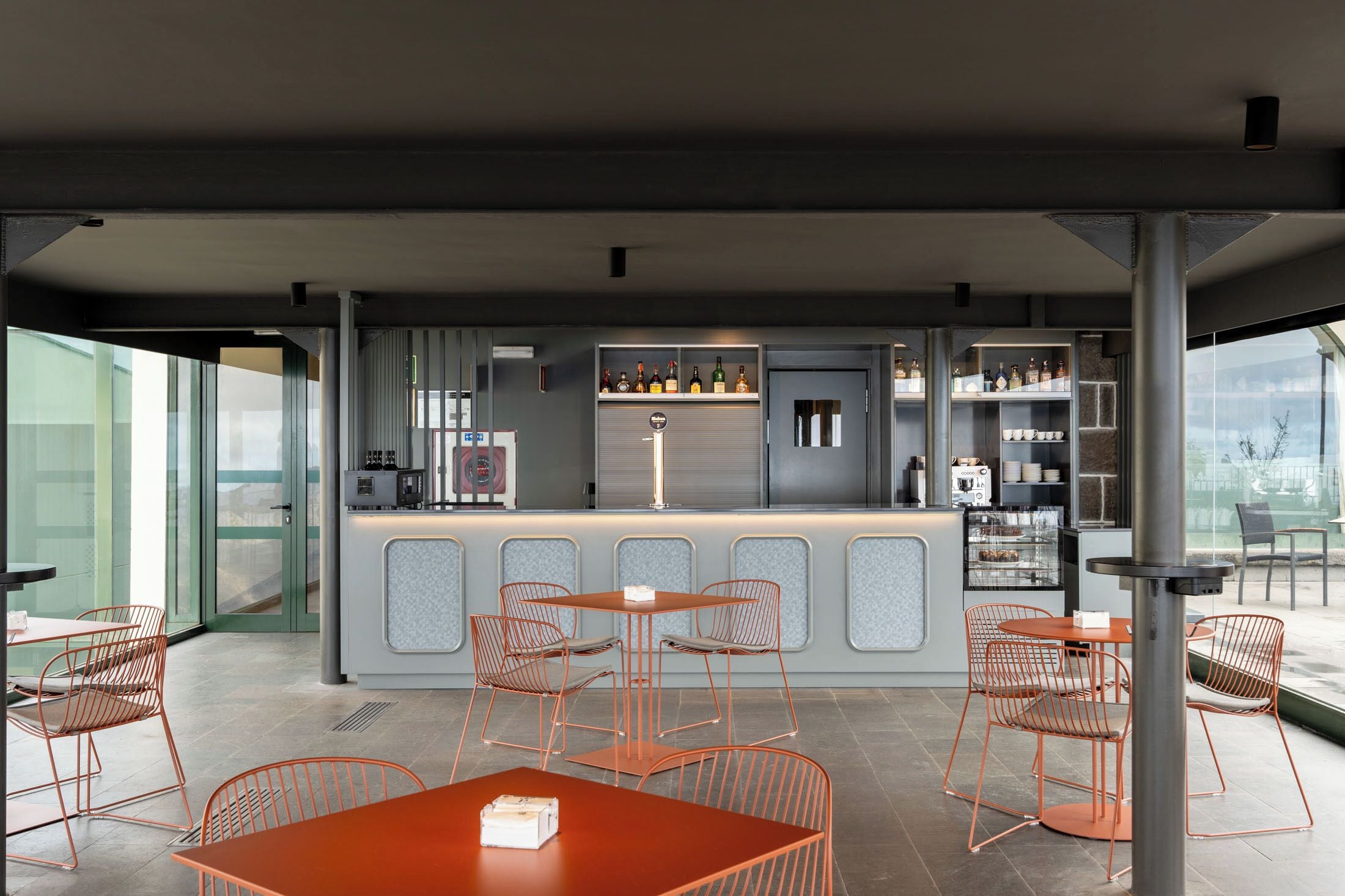 Un espace bar moderne, doté d’un comptoir, de sièges et d’étagères remplies de bouteilles.