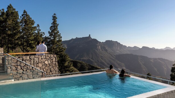 Una piscina con un muro de piedra y una cubierta de madera, con vista a un paisaje montañoso.