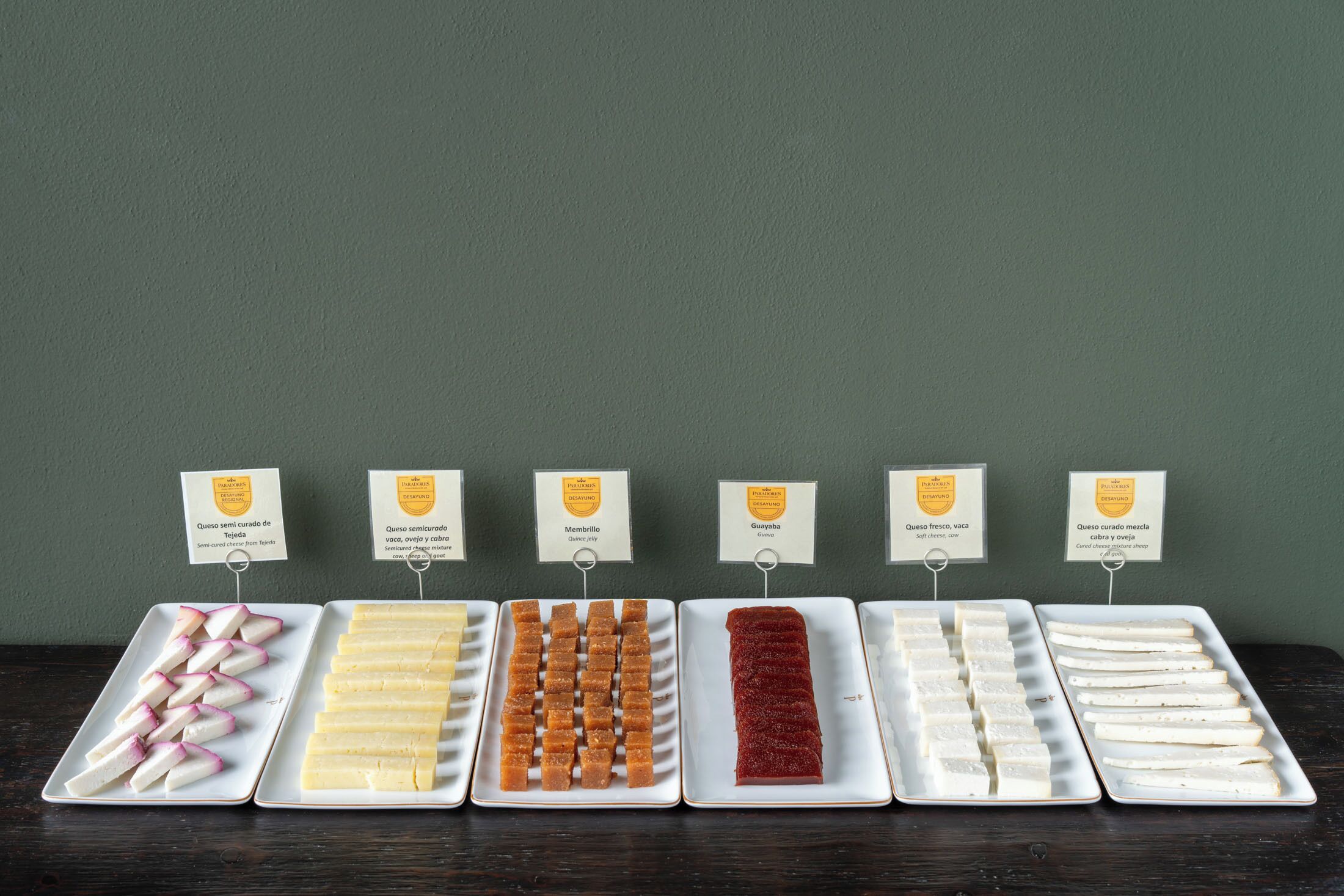 A display of various cheese types on white plates with labels.