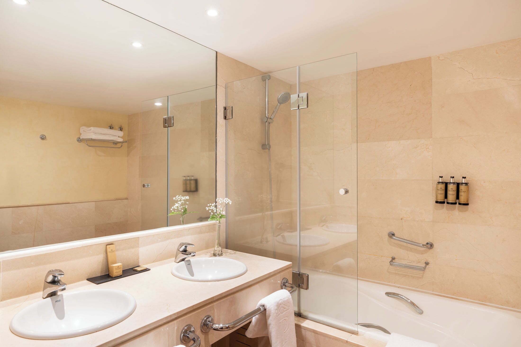A modern bathroom with two sinks, a glass-enclosed shower, and a large mirror.