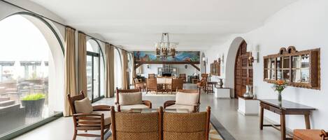 A spacious living area with a large window, a dining table, and several chairs.