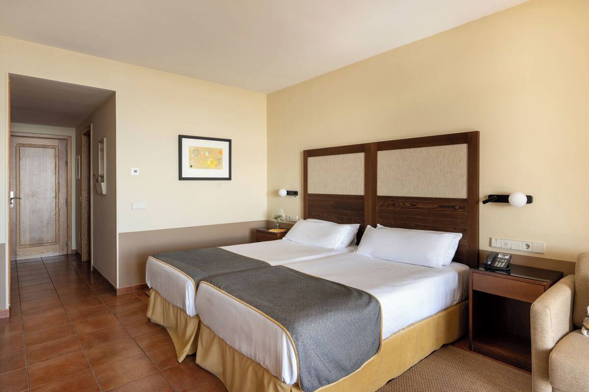 Une chambre d’hôtel avec deux lits, une tête de lit en bois, une table de chevet avec une lampe et une chaise.