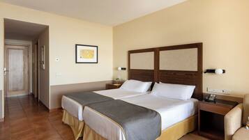 Habitación de hotel con dos camas, cabecero de madera, mesita de noche con lámpara y una silla.
