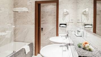 Un baño moderno con pared de mármol, puerta de madera, bañera, dos lavamanos y tocador con espejo.