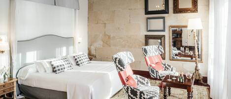 Una habitación de hotel con una cama, dos sillones, una mesita y un espejo.